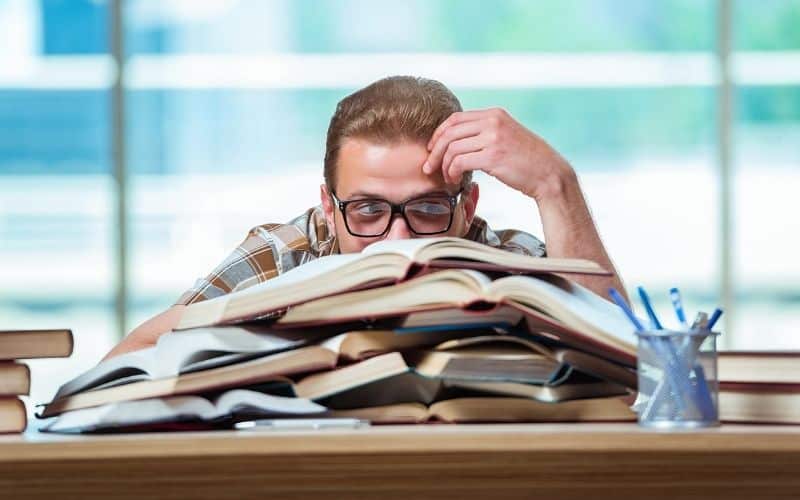male student behind pile of books