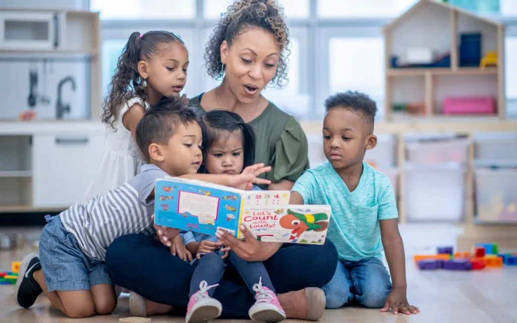 teacher reading a book to four young children