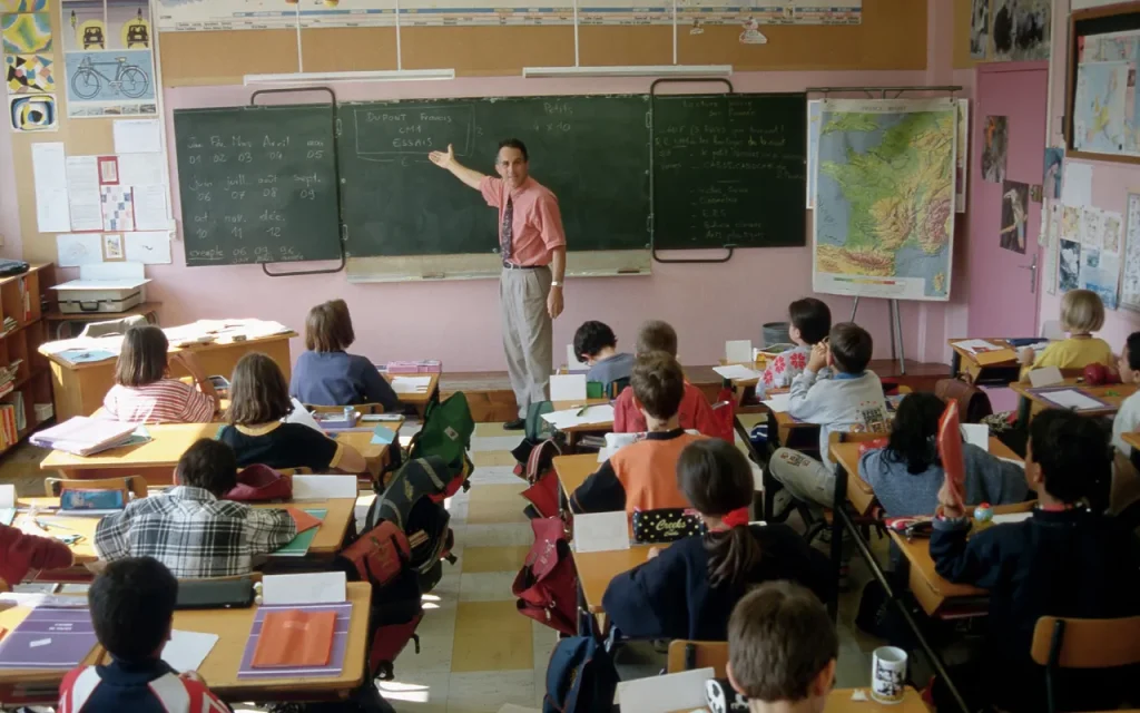 teacher at front of the room pointing at the board in a class full of students