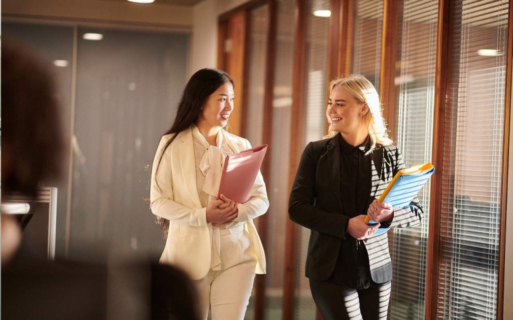 two female law students walk down a corridor, each carrying folders