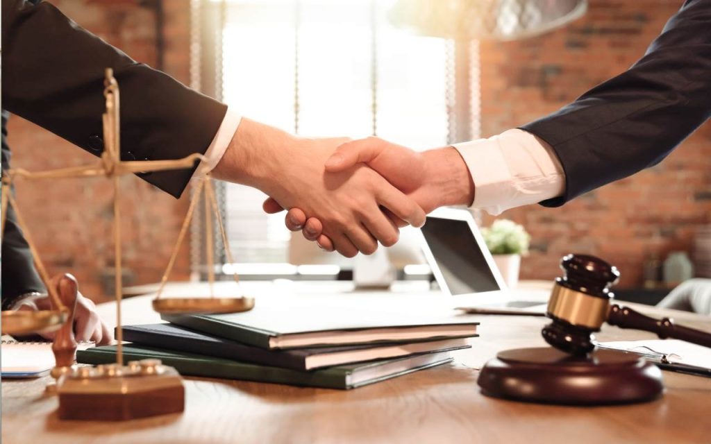 two lawyers shake hands over a gavel and scale on a desk