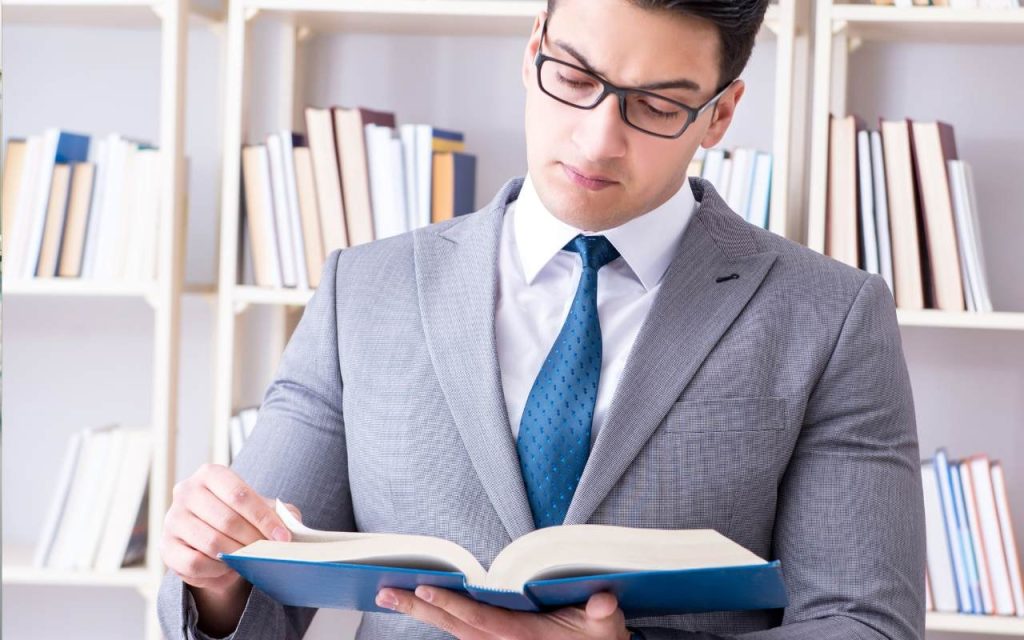 male law student in gray blazer in front of bookshelf