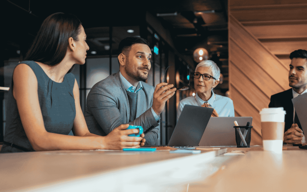 four business executives in a meeting room with wood accent wall