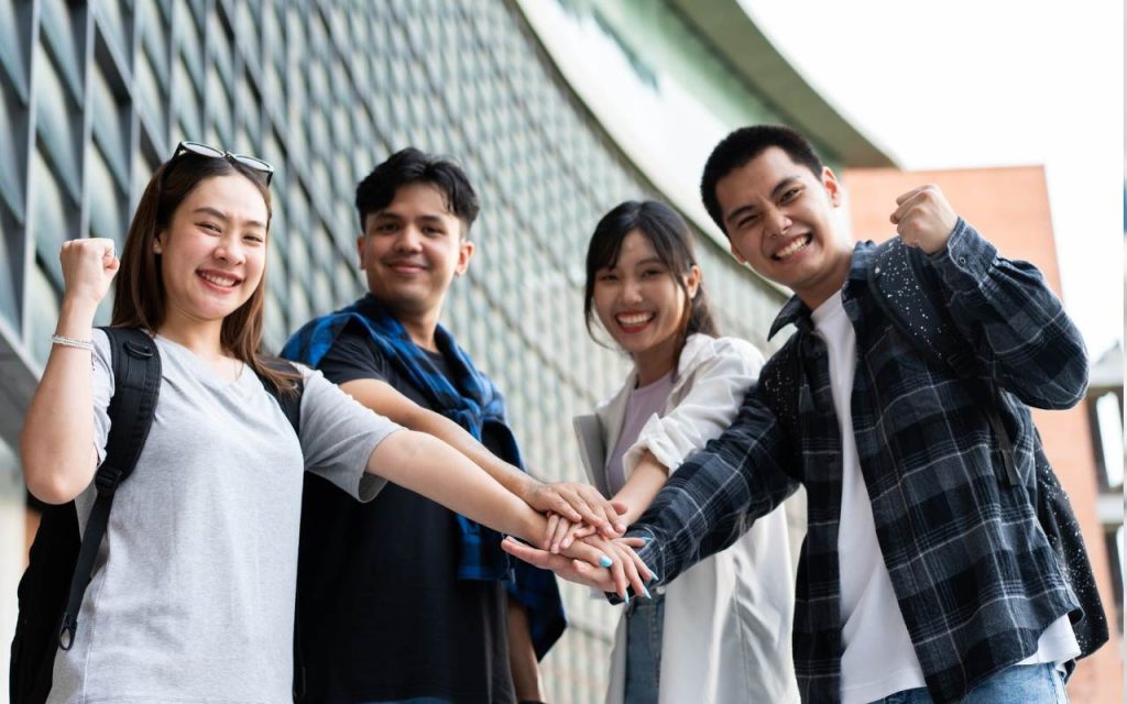 four students put their hands together in front of glass building