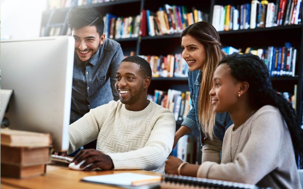 diverse students in the library looking at desktop monitor