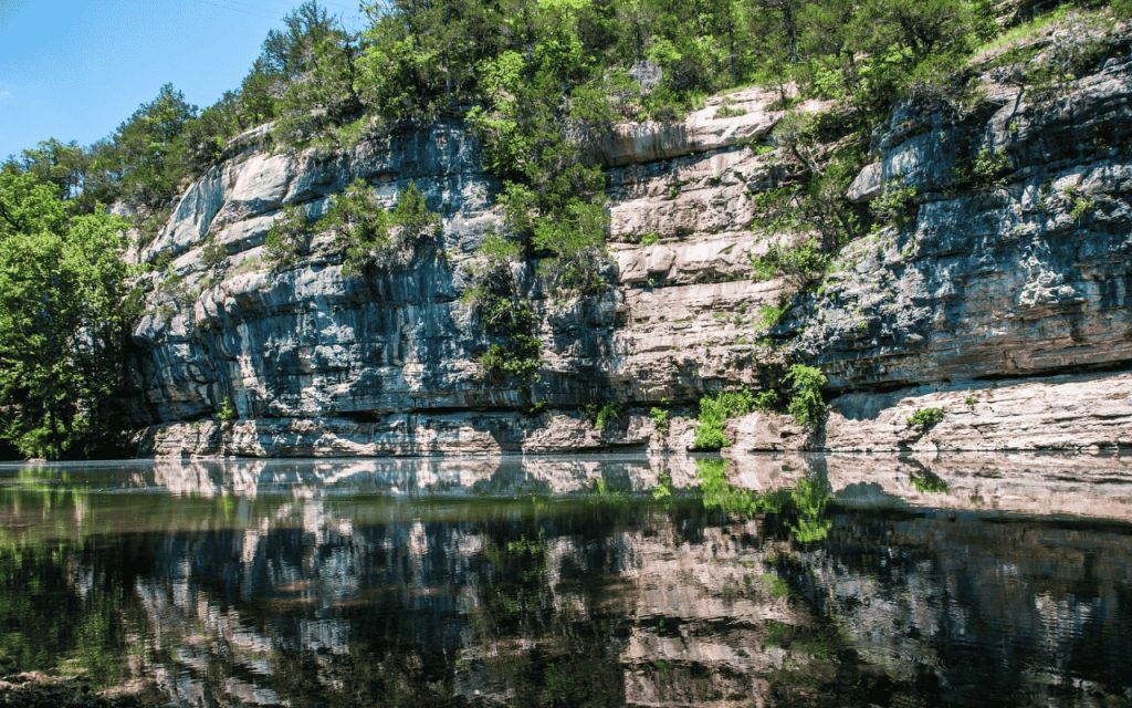 cliff with vegetation reflected in lake