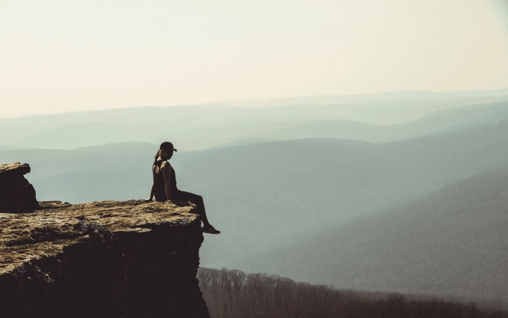 woman sits on the edge of a cliff overlooking woods