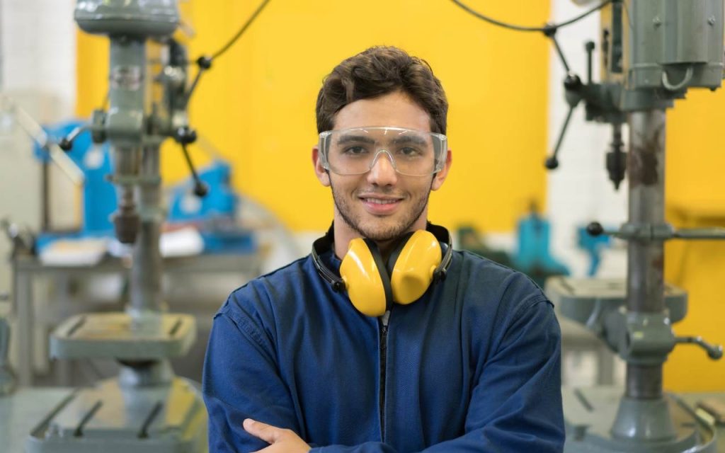 engineering student stand in front of machinery and yellow background