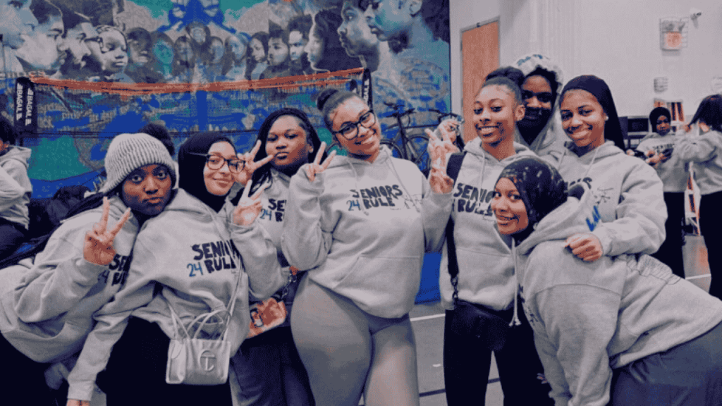 female students of color smile and pose in front of a school poster