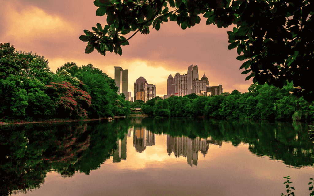 city skyline reflected in lake, framed by green trees