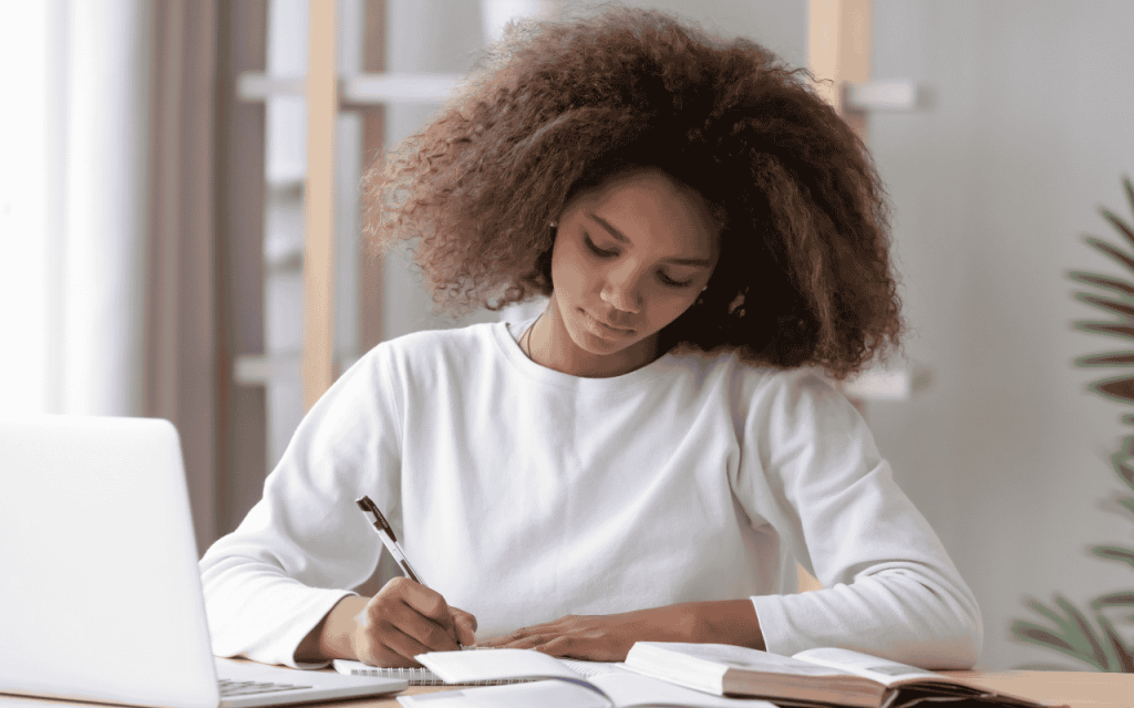 student in white shirt with curly hair writes in a journal