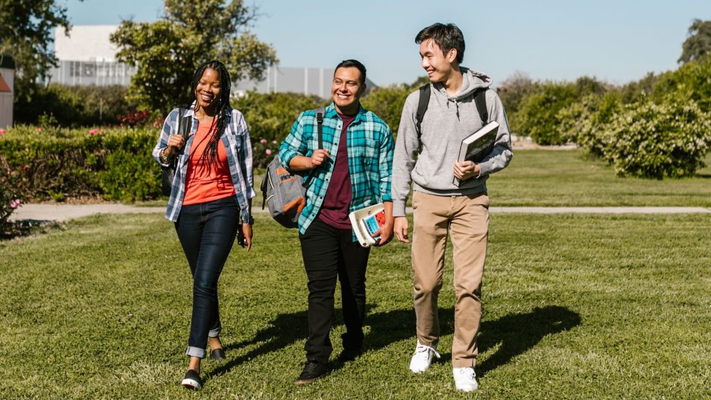 three students walk across college campus with textbooks