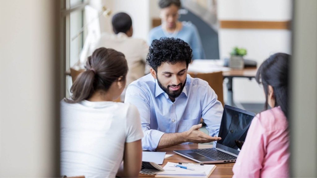 man with laptop sits across from two women