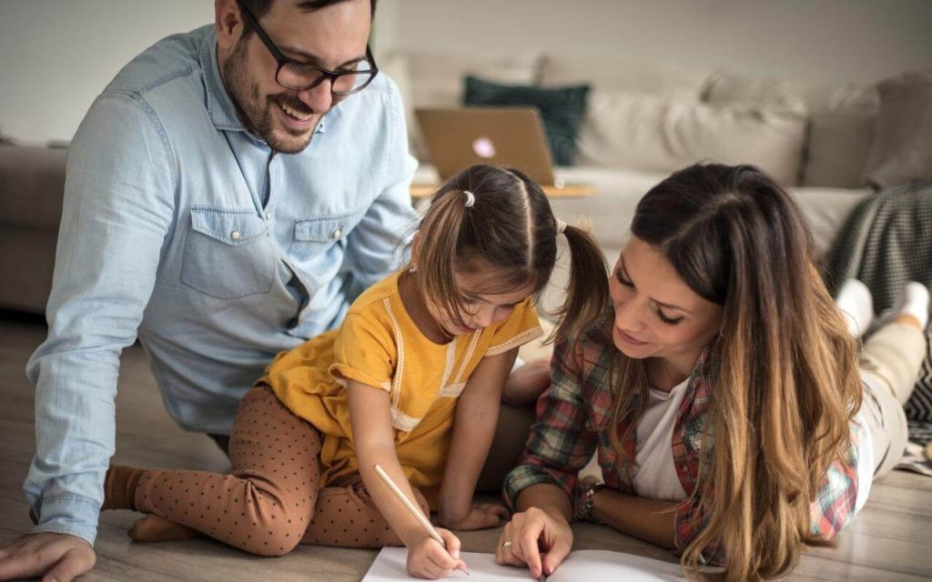 parents with their young daughter drawing on the floor