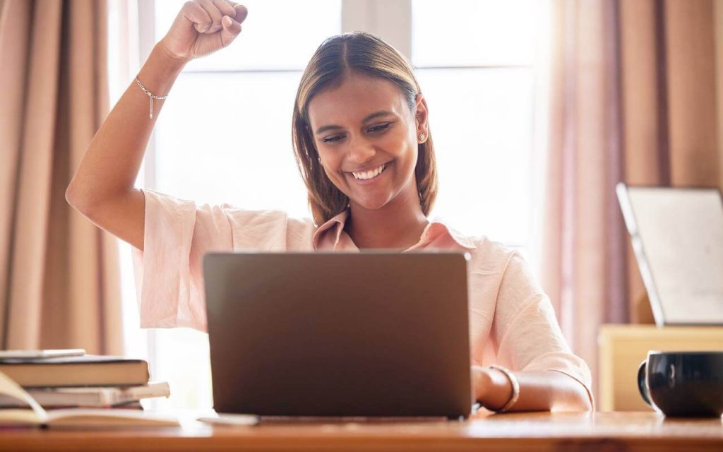 triumphant woman at laptop raises fist in the air